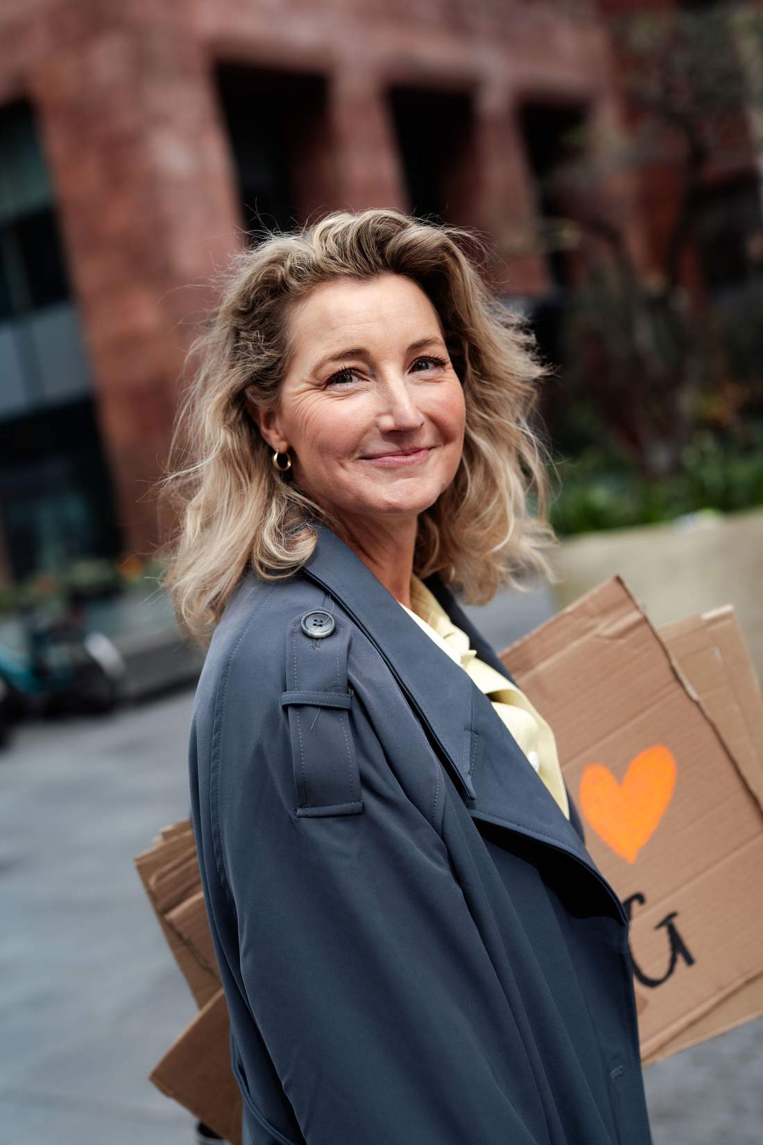Dian in een donkerblauwe jas, met een kartonnen bord met een oranje hart