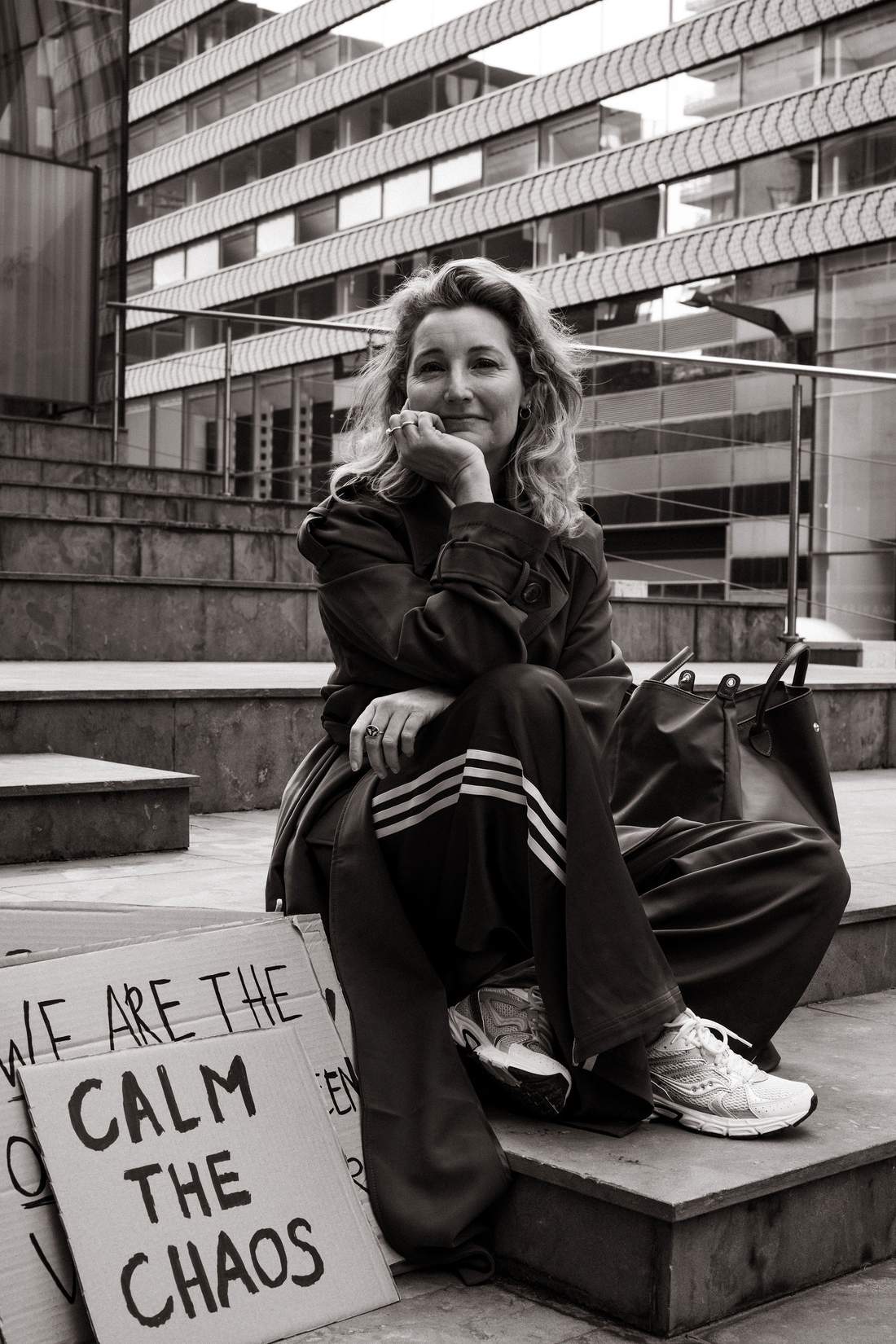 Zwart-witfoto van Dian op een trap in de stad, met het bord I calm the chaos